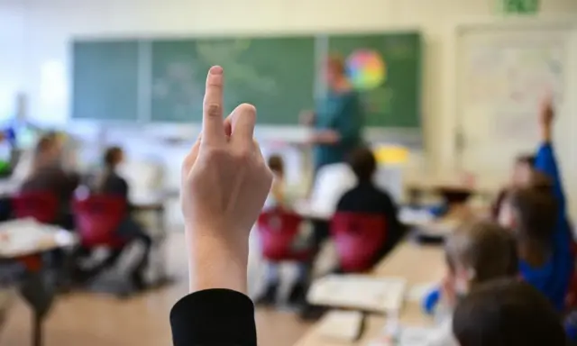 Ein Schüler hebt die Hand, um eine Frage zu stellen. Wie lange muss man in die Schule gehen? Die Antwort liegt im Unterricht.