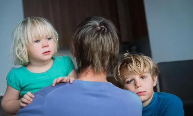 Zwei Kinder blicken besorgt über die Schulter einer Person. Die **Trennung wegen unterschiedlicher Erziehung** scheint sie zu belasten.