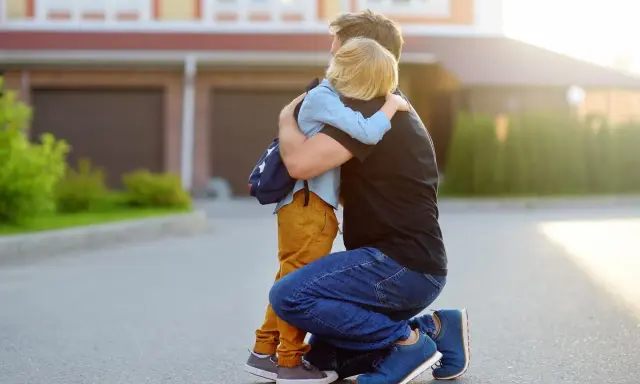 Vater umarmt seinen Sohn mit Rucksack. Ein guter Schulstart nach den Ferien beginnt mit einer liebevollen Umarmung.