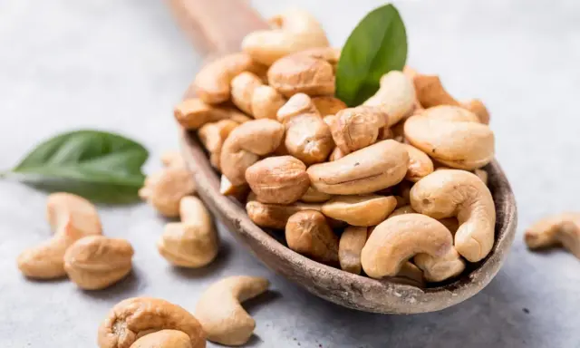 Holzkelle voller Cashewkerne, ideal für die Schwangerschaft. Zwei grüne Blätter liegen daneben.
