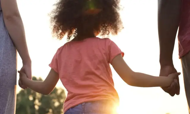 Kind hält Hände von Eltern. Die gesetzliche Regelung Kinderbetreuung Trennung soll das Wohl des Kindes sichern.