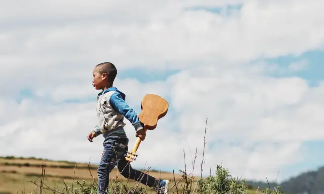 Ein kleiner Junge, vielleicht 18 Monate, rennt mit einer Ukulele durch die Natur. Ein sehr anstrengender, aber glücklicher Moment.