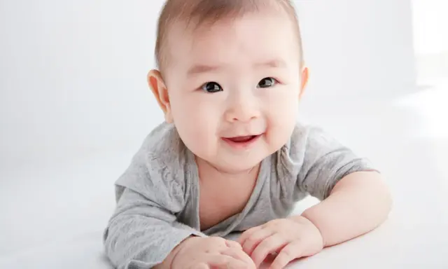 Lächelndes Baby in grauem Shirt auf weißem Hintergrund.