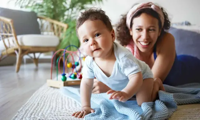 Ein Baby krabbelt neugierig, seine Mutter lächelt. Ein starker Wille zeigt sich schon früh, die Bedeutung des Namens wird gelebt.
