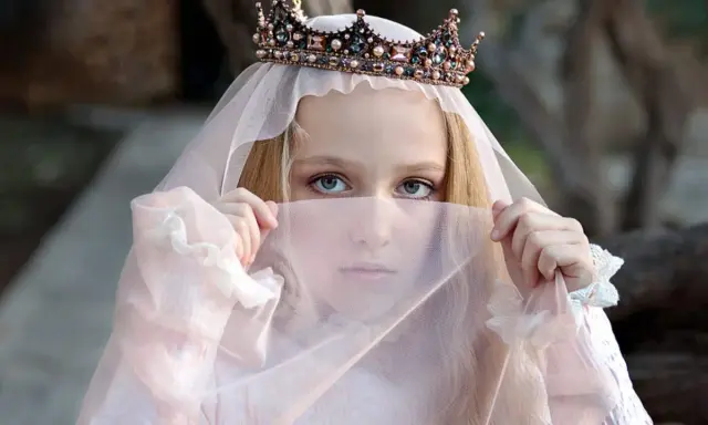 Ein Mädchen mit Krone und Schleier, wie eine Prinzessin aus Herr der Ringe Namen weiblich, blickt geheimnisvoll hervor.