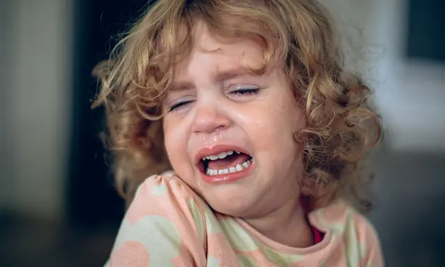 Ein kleines Mädchen mit lockigen Haaren weint bitterlich. Tränen laufen über ihr Gesicht, die Augen sind geschlossen. Ein Ausdruck von starkem **Wut bei Kindern** ist deutlich zu sehen.