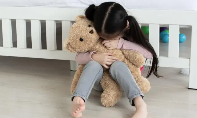 Ein trauriges Kind umarmt seinen Teddybär. Tipps, was tun gegen heimweh kinder, um Trost zu spenden.
