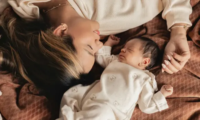 Mutter und Baby liegen eng beieinander. Die Mutter schaut liebevoll auf ihr schlafendes Kind. Ein Moment der Ruhe und Geborgenheit, der die **Baby-Begrenzung beim Schlafen** symbolisiert.