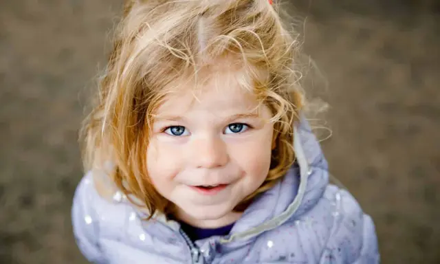 Ein blondes Mädchen mit blauen Augen lächelt. Ihr Haar ist zerzaust, wie bei vielen norddeutschen Frauennamen, die oft eine natürliche Schönheit widerspiegeln.