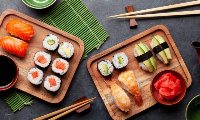 Frischer roher Fisch stillt den Appetit auf Sushi. Nigiri mit Lachs, Maki-Rollen mit Avocado und Garnelen-Sushi auf Holzbrettern.