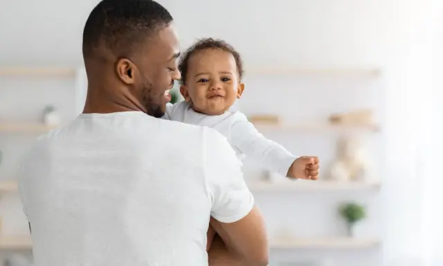 Ein Vater hält sein lächelndes Baby. Vielleicht sucht er nach christlichen Jungennamen für seinen kleinen Schatz.