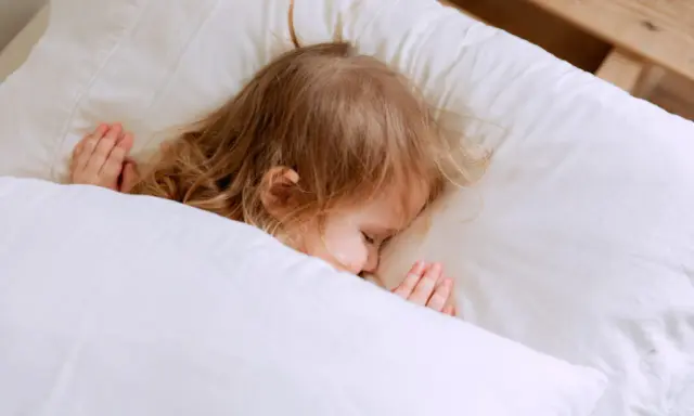 Kleines Kind schläft friedlich im Bett. Ab wann schlafen Kinder alleine ein? Diese süße Szene zeigt einen friedlichen Schlaf.
