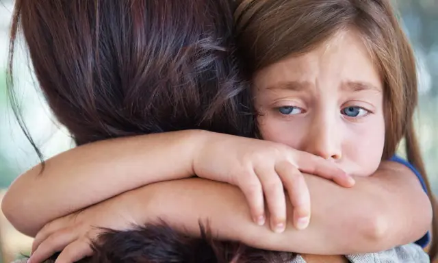 Ein trauriges Kind umarmt seine Mutter. In der Grundschule darf das Kind nicht mitspielen, es fühlt sich ausgeschlossen.