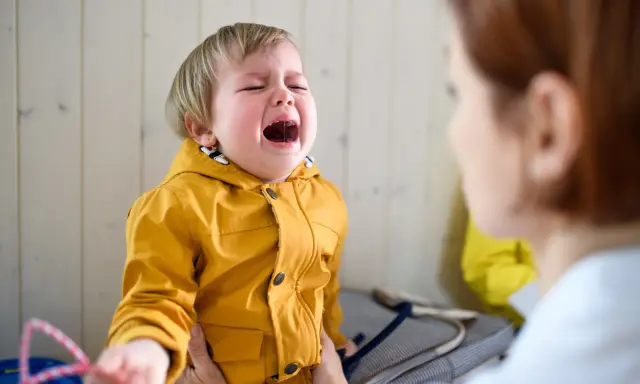 Ein weinendes Kind im Kindergarten, das nach Mama ruft. Die Erzieherin versucht, das kleine Mädchen zu trösten.