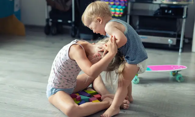 Ein aggressives Kind hält das Haar eines anderen Kindes, das auf bunten Holzklötzen sitzt.