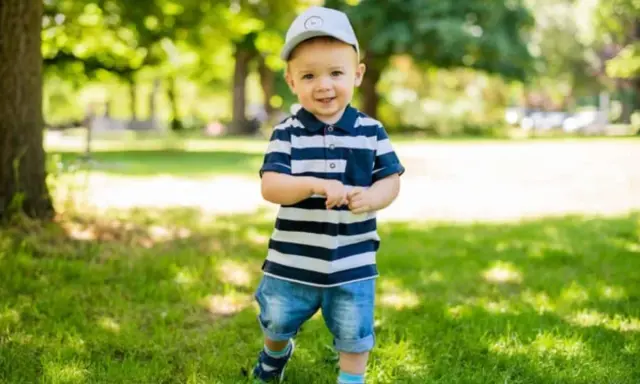 Ein lächelnder Junge mit Kappe und gestreiftem Polo-Shirt im Park. Vielleicht heißt er Finn, Leo oder Noah – beliebte Jungennamen mit 4 Buchstaben.