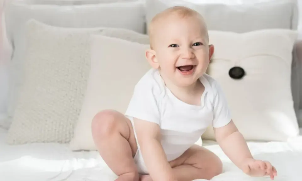 Ein strahlendes Baby, ein echtes Kind der Sonne, sitzt auf einem Bett. Elias' Lachen ist ansteckend.