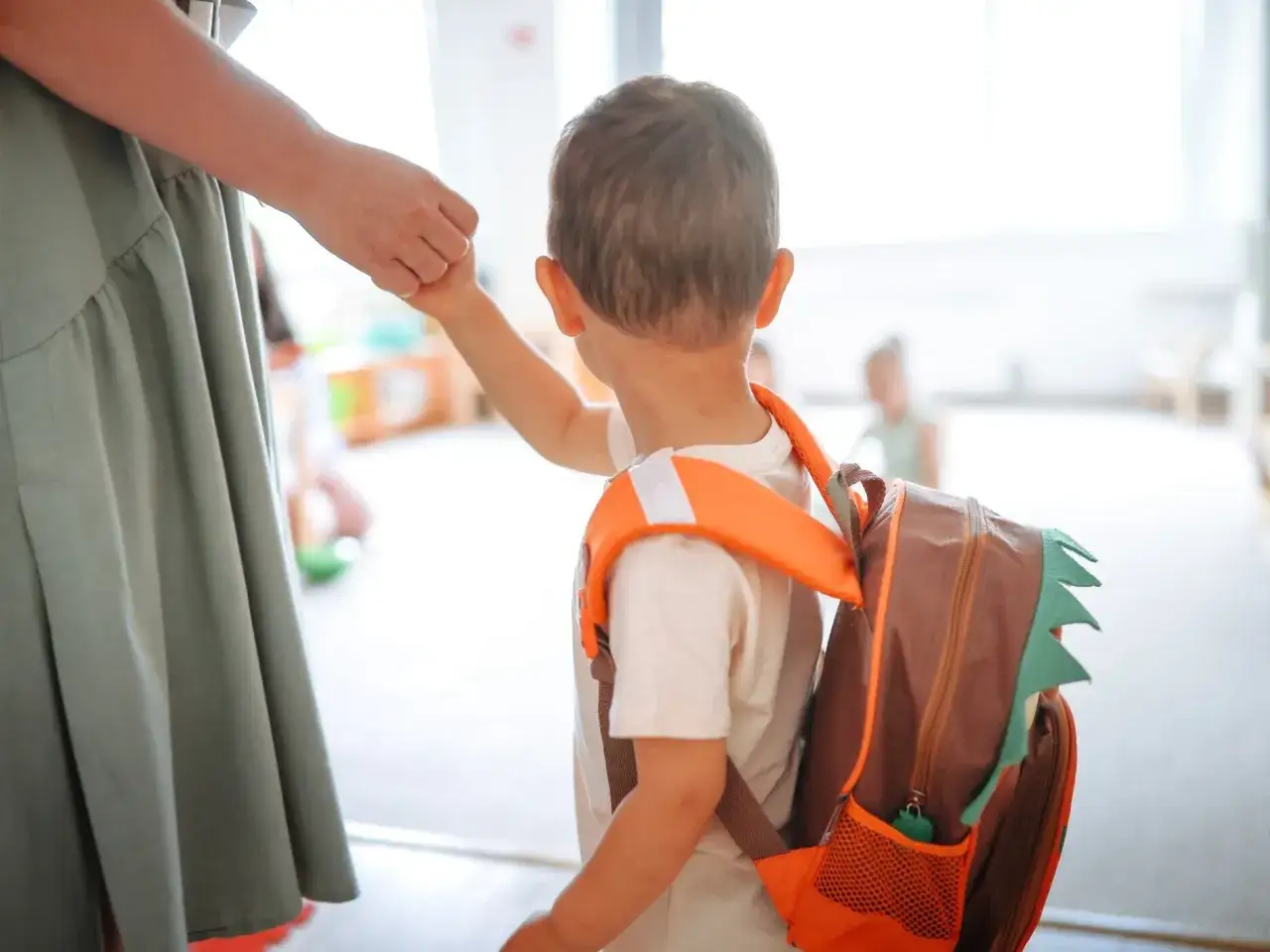 Ein Kind mit Rucksack wird in die Schule gebracht. Die Eltern halten H&auml;ndchen, um den &Uuml;bergang zu erleichtern, auch wenn es um Windeln in der Schule geht.