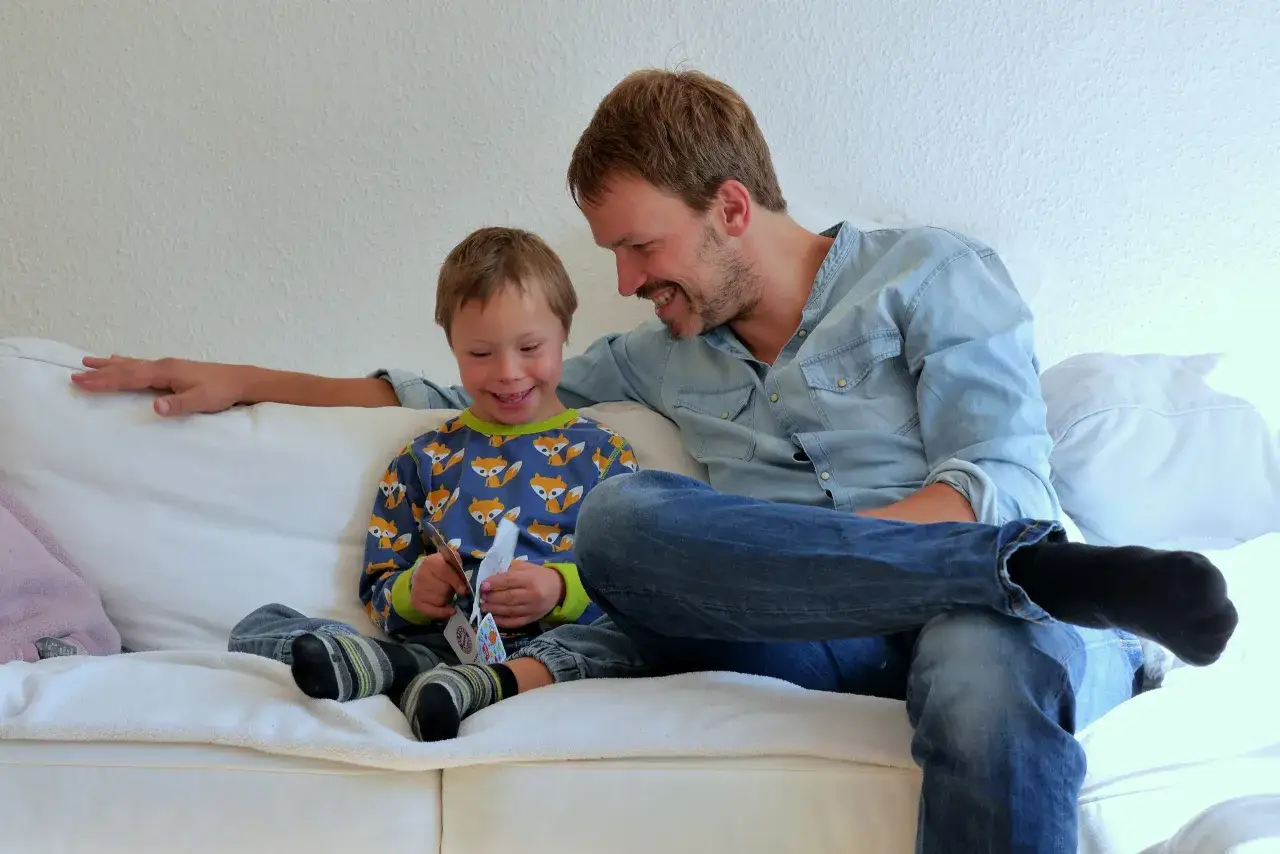 Ein Vater und sein Sohn lachen gemeinsam auf dem Sofa. Das zeigt, was einen guten Vater ausmacht: Liebe, Geduld und gemeinsame Freude.