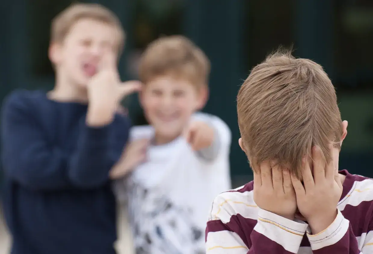 Ein Junge versteckt sein Gesicht, w&auml;hrend zwei andere ihn verspotten. Ein trauriges Bild von Konflikten in der Schule.