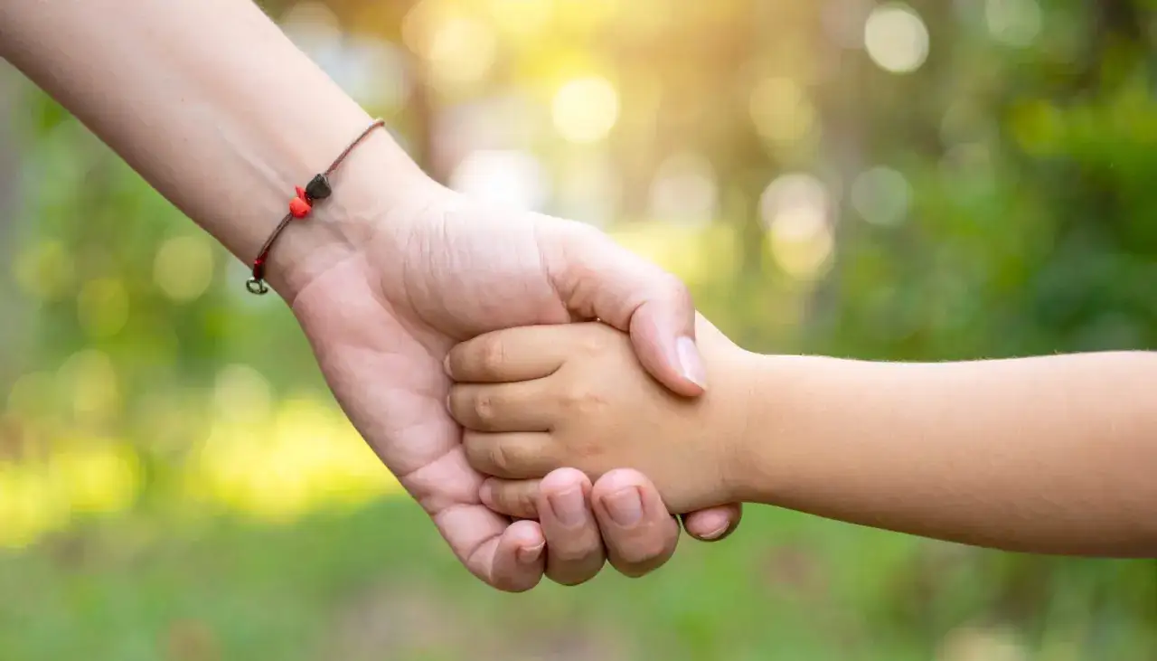 Eine Hand hält die Hand eines Kindes. Das Band am Handgelenk der Erwachsenen erinnert daran, dass das Leben vergänglich ist, aber Liebe bleibt. Was bedeutet tot?