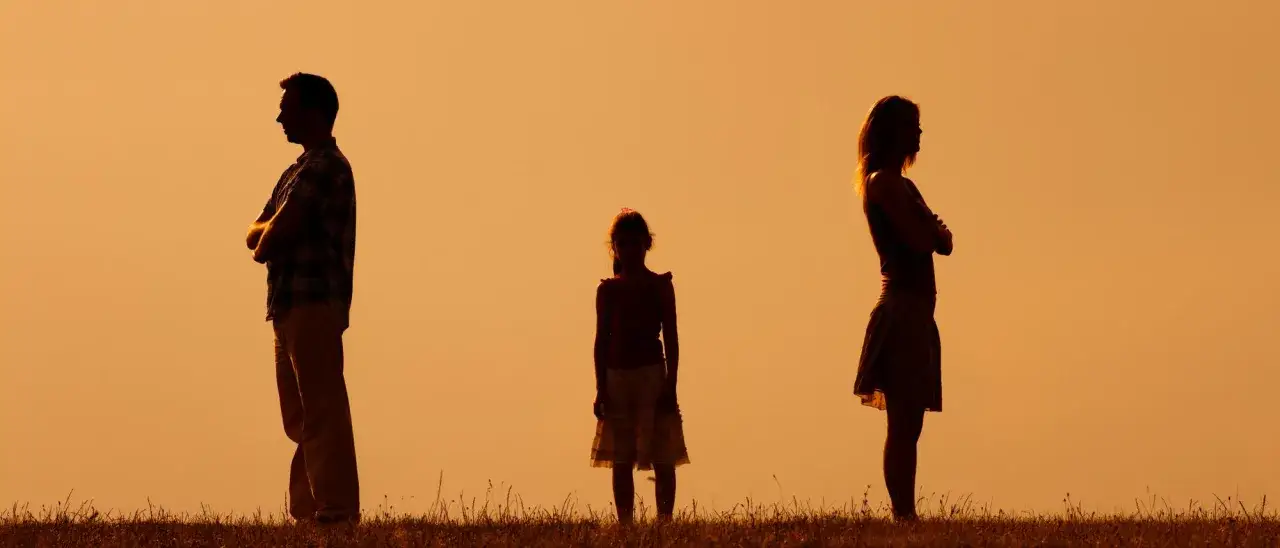 Silhouetten von Eltern, die sich voneinander abwenden, während ein Kind dazwischen steht. Ein Bild, das die Herausforderungen einer Trennung mit Kindern symbolisiert.