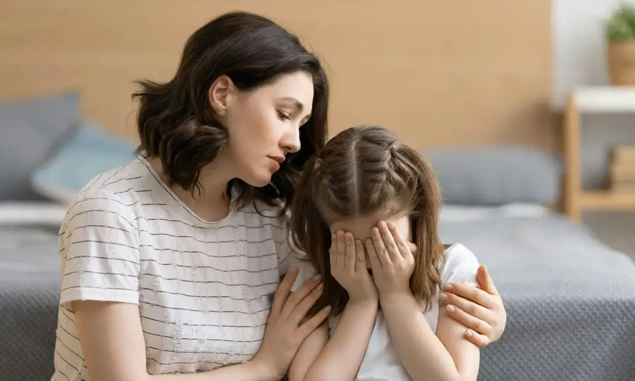 Eine Mutter tr&ouml;stet ihr weinendes Kind, das sich die Augen zuh&auml;lt. Sie leidet unter Zwangsgedanken bei Kindern und braucht Unterst&uuml;tzung.