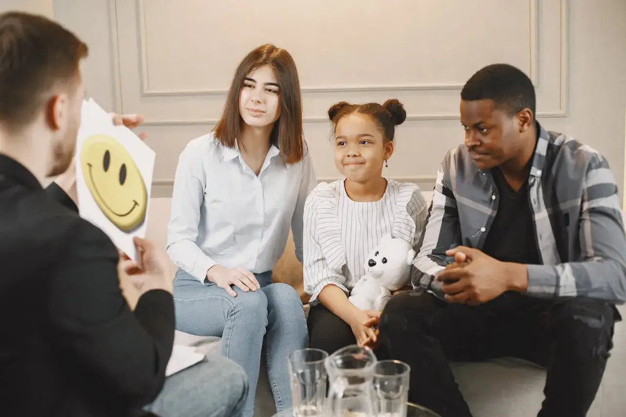 Familie bespricht, warum ein Kind nicht zur Schule geht und welche Konsequenzen das hat. Ein Mann h&auml;lt ein Bild mit einem Smiley hoch.