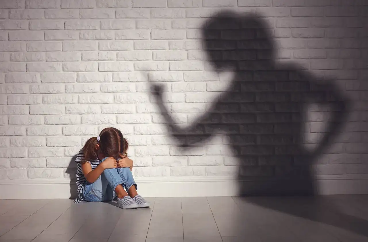Ein Mädchen kauert weinend auf dem Boden, während ein bedrohlicher Schatten einer erwachsenen Person an der Wand erscheint. Psychologie: Mutter hasst Tochter?