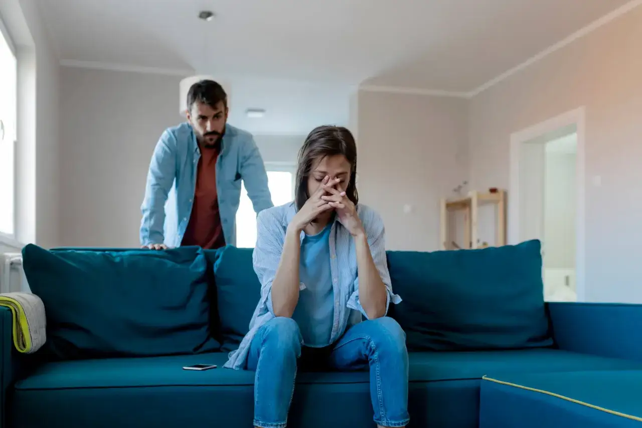 Traurige Frau sitzt auf Sofa, Mann steht dahinter. Sie fragt sich, wie sage ich meinen Kindern, dass wir uns trennen.