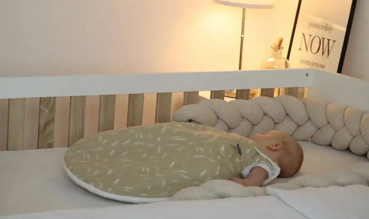Ein Baby schl&auml;ft friedlich in seinem Bettchen, eingeh&uuml;llt in einen gem&uuml;tlichen Schlafsack. Die weiche Bettumrandung bietet zus&auml;tzliche baby begrenzung schlafen und Geborgenheit.
