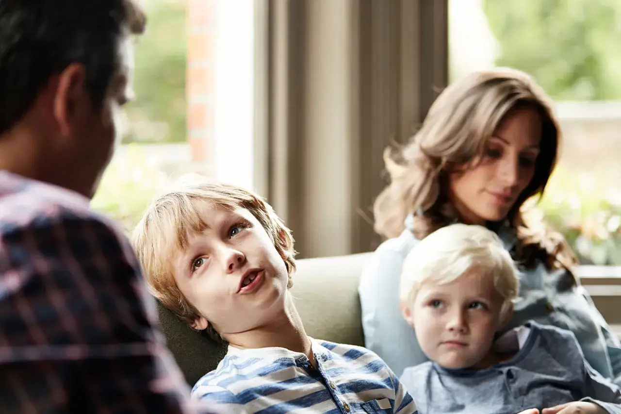 Ein Junge spricht mit seinem Vater, während seine Mutter und sein jüngerer Bruder im Hintergrund sitzen. Eine Szene, die zeigt, wie Kinder mit der Situation umgehen, wenn sich Eltern trennen.