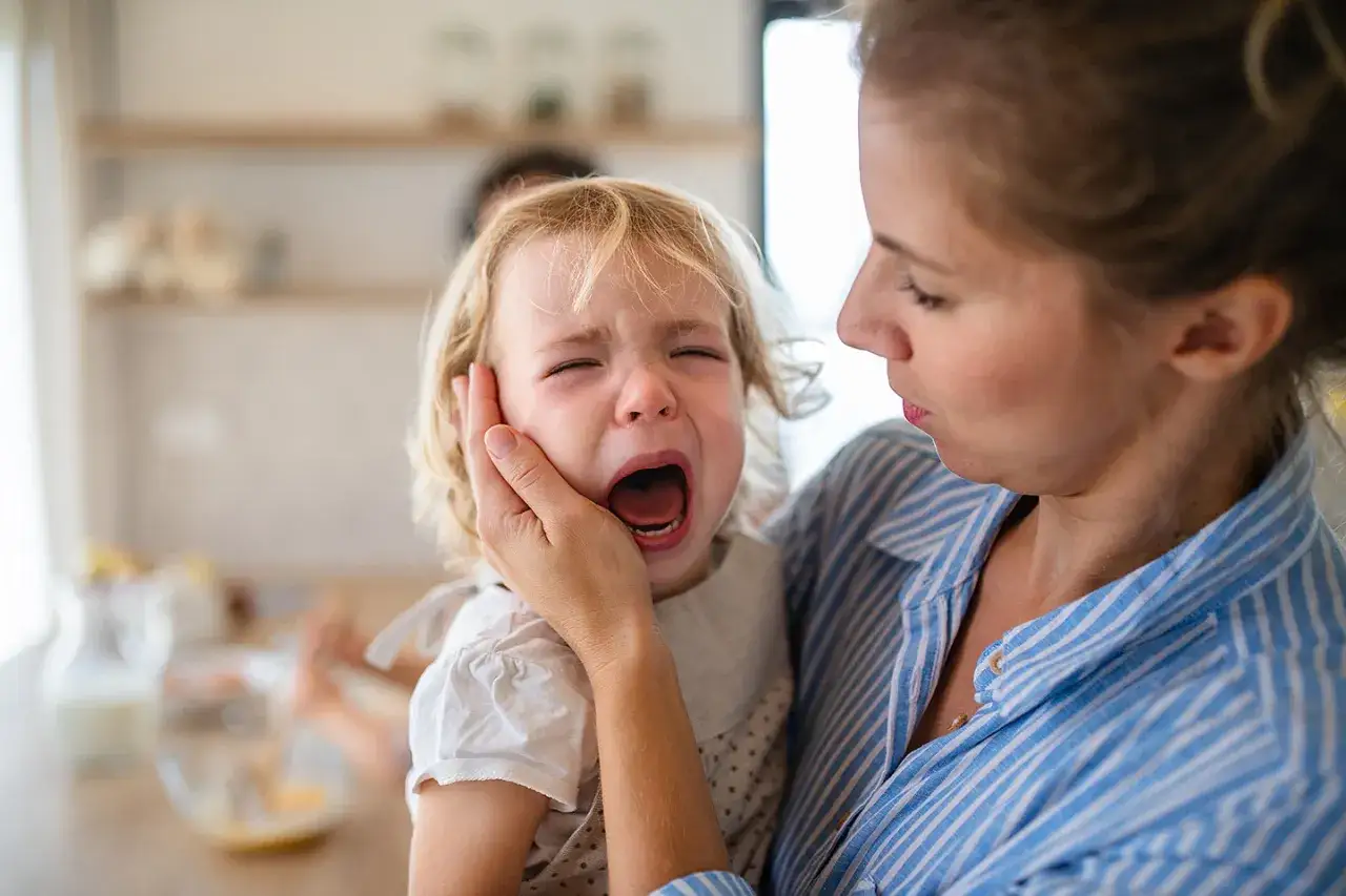 Mutter tröstet weinendes Kind. Der Wut bei Kindern Ausdruck ist deutlich zu sehen, während die Mutter versucht zu beruhigen.