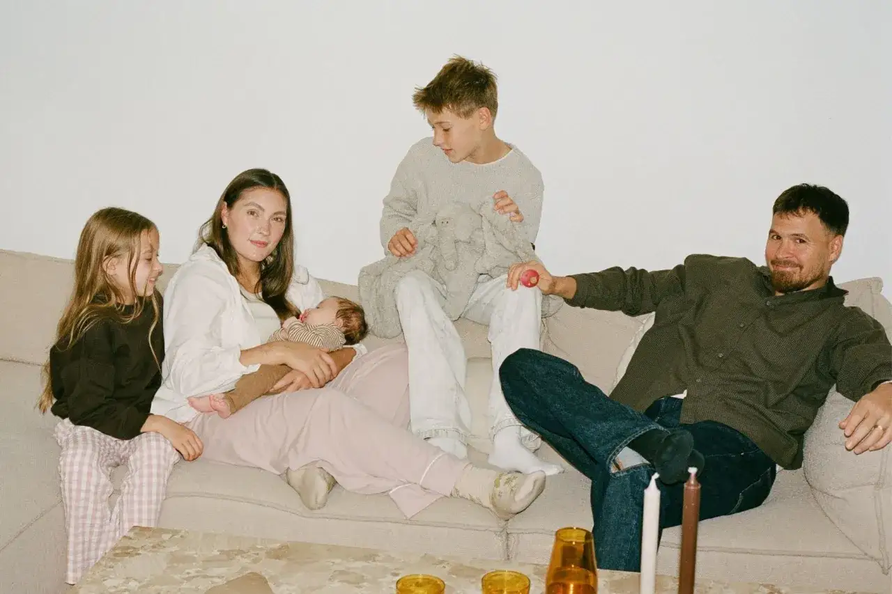 Familie auf Sofa: Mutter mit Baby, zwei Kinder, Vater. War das dritte Kind eine falsche Entscheidung?