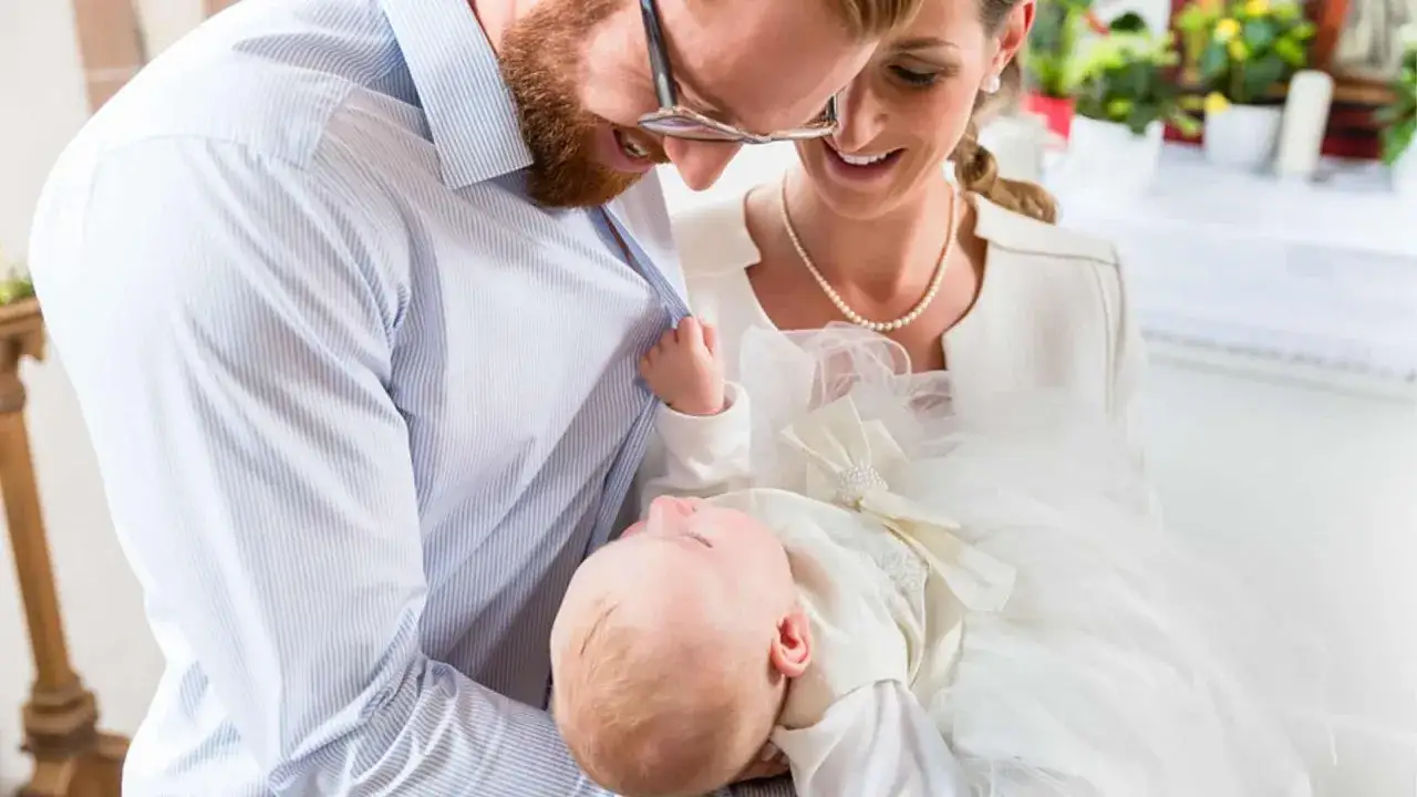 Eltern halten ihr Baby im Taufkleid. Ein sch&ouml;ner Moment, der an christliche Jungennamen wie David oder Elias erinnert.