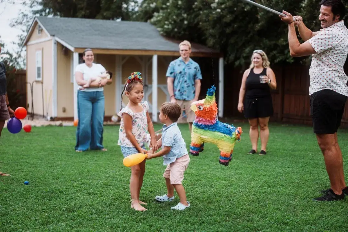Ein bunter Pi&ntilde;ata-Esel h&auml;ngt im Garten. Ein M&auml;dchen und ihr kleiner Bruder halten sich an den H&auml;nden, ihre bruder und schwester liebe ist sp&uuml;rbar.