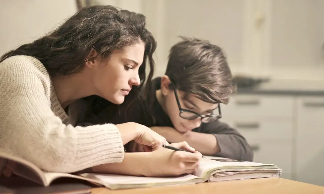 Geduld ist gefragt, wenn das Kind nicht lernen will. Eine Frau erklärt einem Jungen mit Brille konzentriert eine Aufgabe in einem Buch.