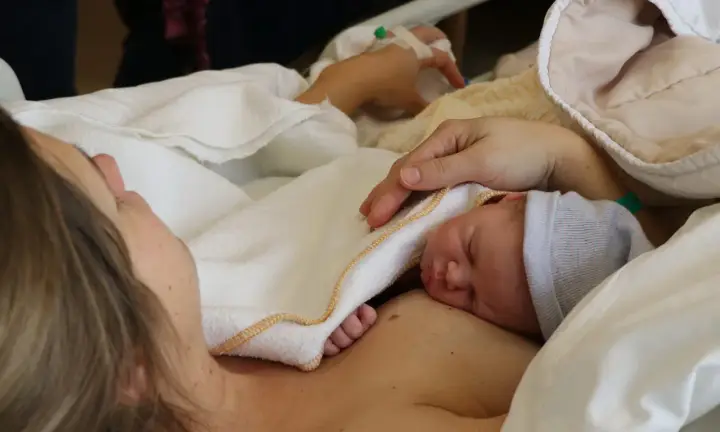 Ein kleiner Sternengucker-Baby schläft auf der Brust seiner Mutter, eingewickelt in eine weiche Decke.