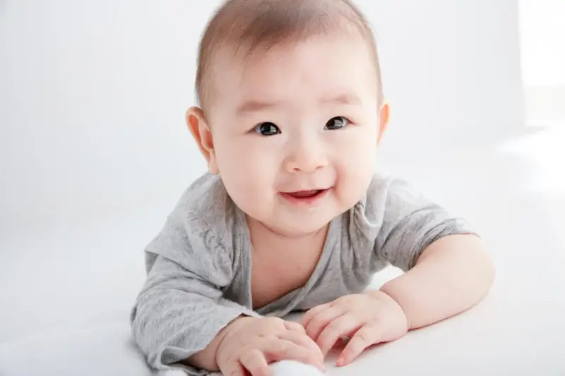 Lächelndes Baby in grauem Shirt auf weißem Hintergrund.